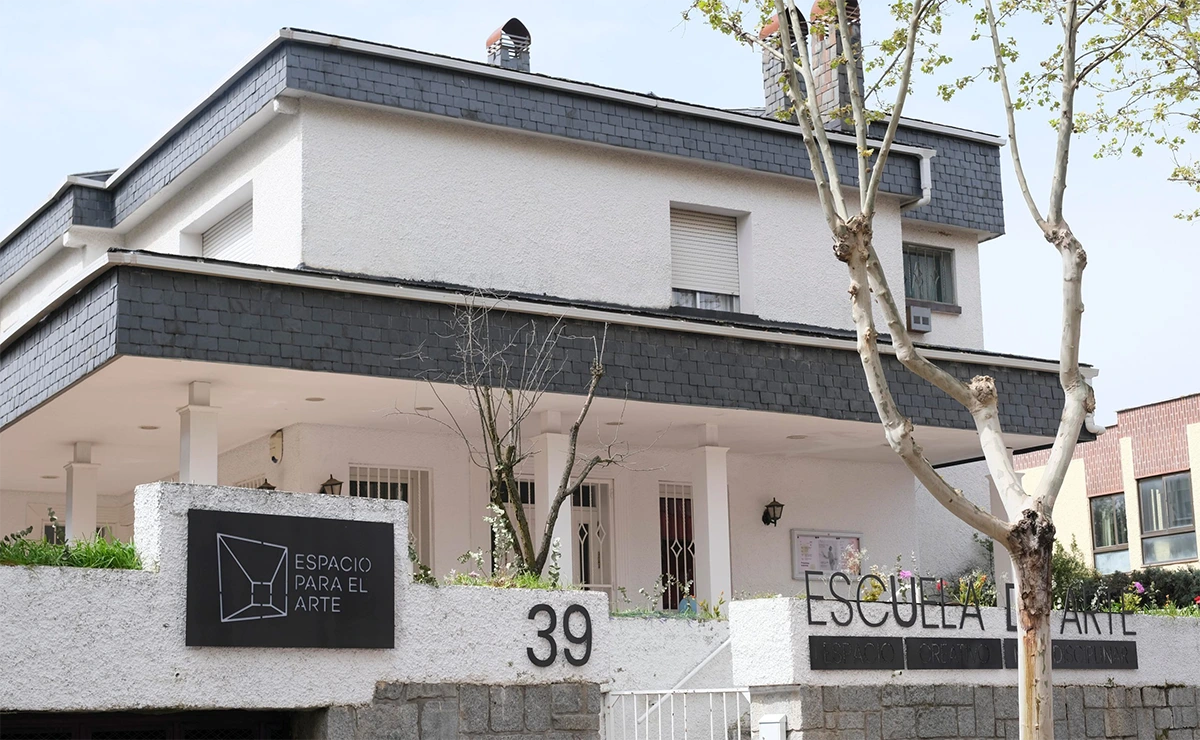 Foto exterior del local de Espacio para el Arte en Torrelodones. La foto fue tomada durante un día otoñal, donde la luz resalta los blancos de las paredes y el cartel del espacio en la fachada.